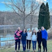 Six people standing outdoors in front of a lake.