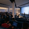 Man holding a pointer who is lecturing in front of a full room.