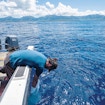 A photograph of a person riding a boat in the ocean and reaching into the water.