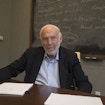 Jim Simons sitting in front of chalkboard.