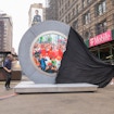 A large black sheet is being pulled of a silver circular structure in New York City