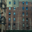 Boy sitting on on the steps of the fire escape surrounded by brick apartment buildings