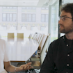 Two people conversing in a business boardroom. One of the people is smiling while the other has a neutral expression.